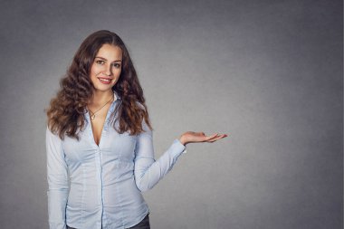 Yakın plan mutlu, güler yüzlü genç bir kadın el kol hareketi yapıyor. Fotokopi alanını açık avuç içiyle, izole edilmiş gri duvar arkaplanı ile sunuyor. Pozitif insani duygu işareti yüz ifadesi