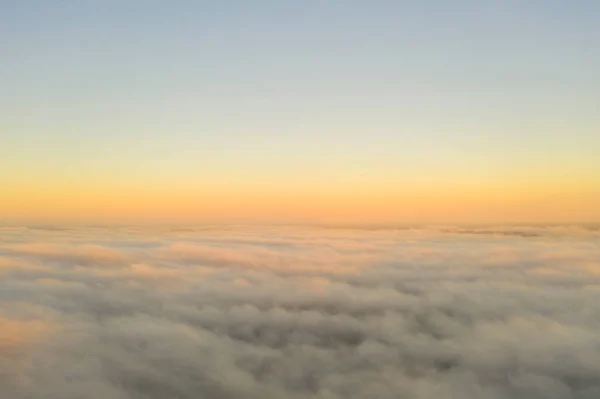 Aerial view gold sunrise over clouds in blue sky. Aerial top view cloudscape. Texture of clouds. View from above. Orange sunrise or sunset over clouds. Panorama clouds texture