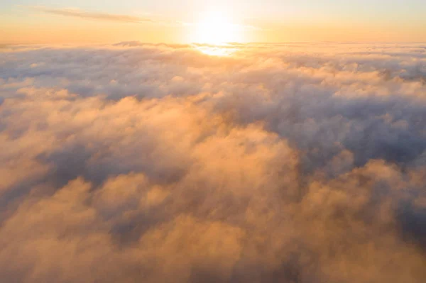 Aerial view gold sunrise over clouds in blue sky. Aerial top view cloudscape. Texture of clouds. View from above. Orange sunrise or sunset over clouds. Panorama clouds texture