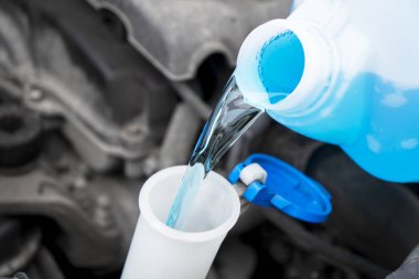 Plastik kutudan araba yıkama sıvısı deposuna sıvı dökülüyor. Ön cam su tankını çamaşır suyuyla kapat.. 