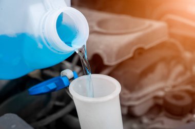 Plastik kutudan araba yıkama sıvısı deposuna sıvı dökülüyor. Ön cam su tankını çamaşır suyuyla kapat..