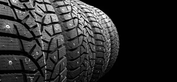 Winter studded tire. Winter car tires isolated on black background. Tire stack background. Tyre protector close up. Square powerful spikes. Black studdable winter tyre profile. Car tires in a row