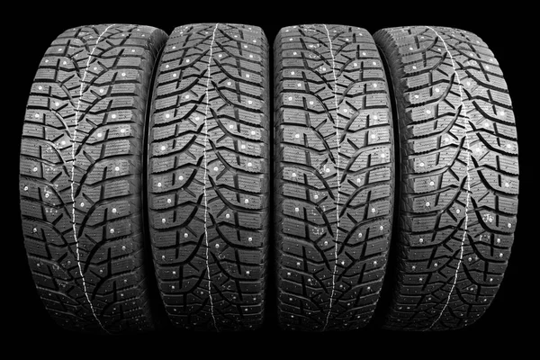 Winter studded tire. Winter car tires isolated on black background. Tire stack background. Tyre protector close up. Square powerful spikes. Black studdable winter tyre profile. Car tires in a row