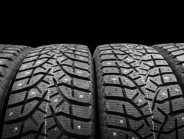 Winter studded tire. Winter car tires isolated on black background. Tire stack background. Tyre protector close up. Square powerful spikes. Black studdable winter tyre profile. Car tires in a row