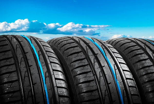 Summer car tires on over blue sky with clouds. Tire stack background. Car tyre protector close up. Black rubber tire. Brand new car tires. Close up black tyre profile. Car tires in a row