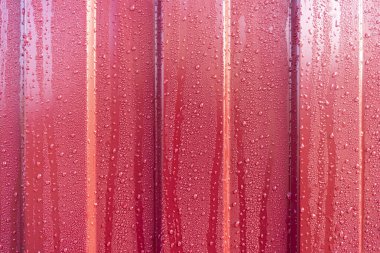 Çatı kaplamasına su damlatılıyor. Kırmızı metal profil yüzeyinde su birikintisi var.