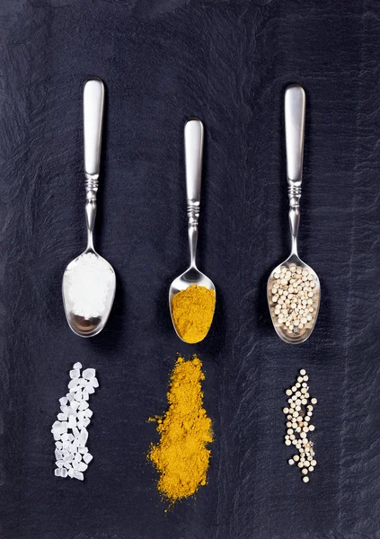 Spoons with a variety of spices spilled on natural black slate s — Stock Photo, Image