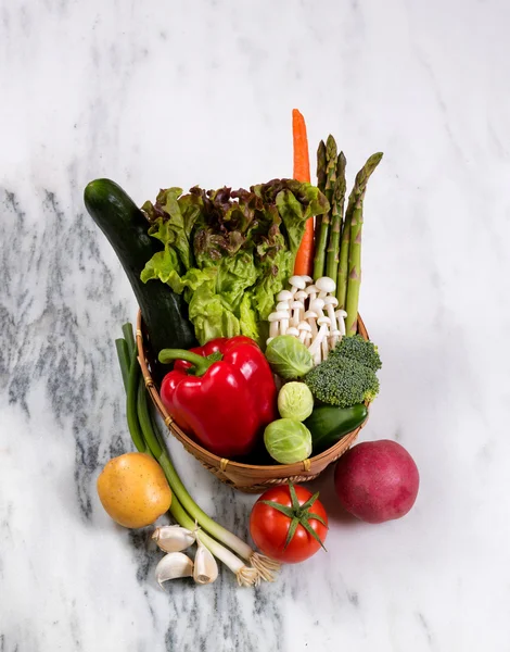 Korg med färska hela grönsaker visas på naturlig marmor sto — Stockfoto
