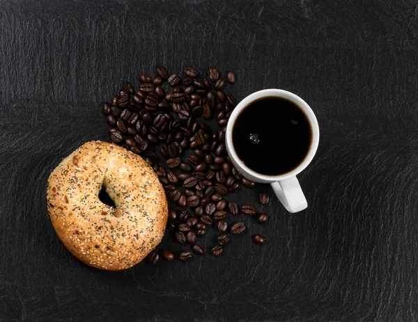 Dark coffee and bagel with roasted beans on natural slate stone — Stock Photo, Image