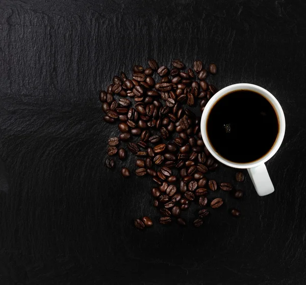 Dark coffee with roasted beans on natural slate stone background — Stock Photo, Image