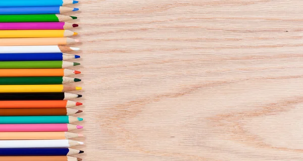 Colorful pencils lined up on oak wooden desktop — Stock Photo, Image