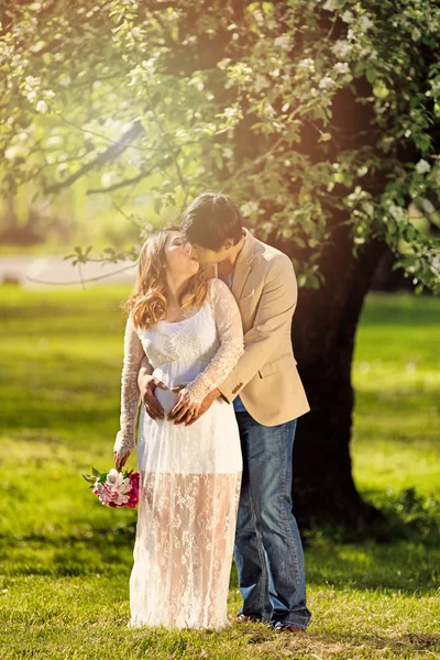 Expecting mom and dad kissing under flowering tree — Stock Photo, Image