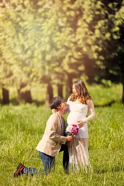 Future dad kneeling to expecting mom with flowers in hand — Stock Photo, Image