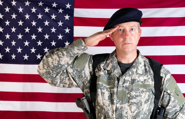 Soldado veterano saludando con bandera de EE.UU. en segundo plano mientras está armado — Foto de Stock