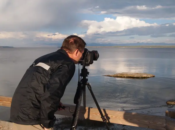 Uomo che scatta foto del lago con macchina fotografica montata su treppiede — Foto Stock