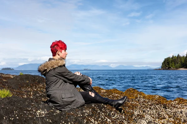 Teen girl thinking while sitting on rock near lake and woods — Stock Photo, Image