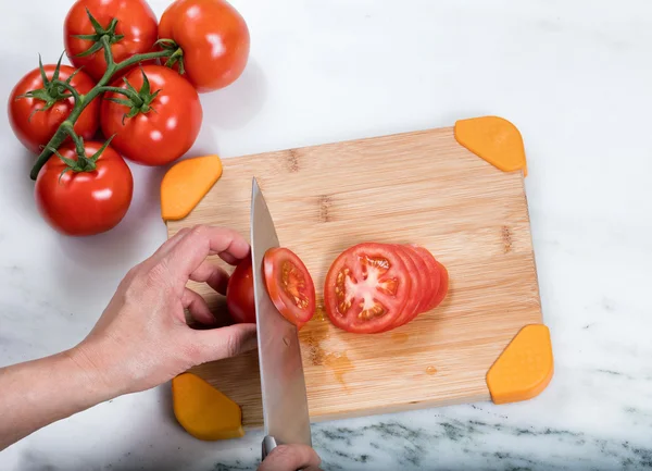 Trancher à la main des tomates fraîches de jardin sur une planche à découper en bambou naturel — Photo