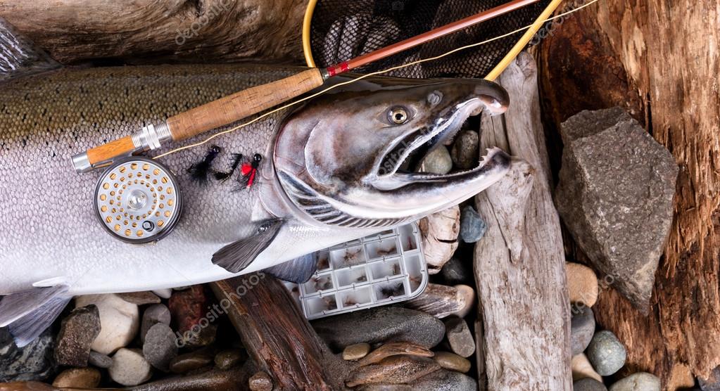 Vintage fly fishing equipment on top of large trout in riverbed