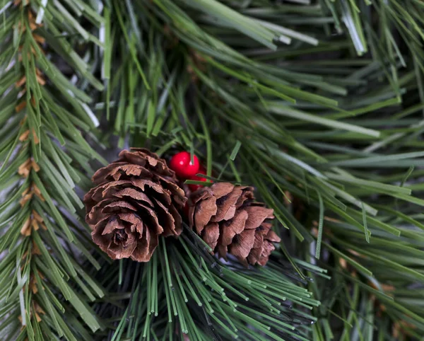 クリスマスシーズンのために常緑樹の枝に囲まれた人工松のコーンと赤い果実の終わり — ストック写真