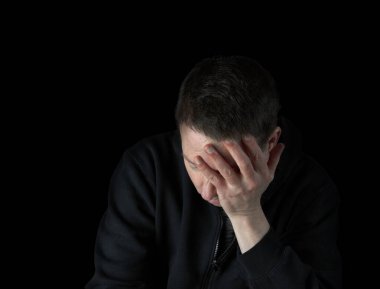 Siyah bir kazak giymiş depresif, olgun bir adam karanlıkta yüzünü tutuyor. 