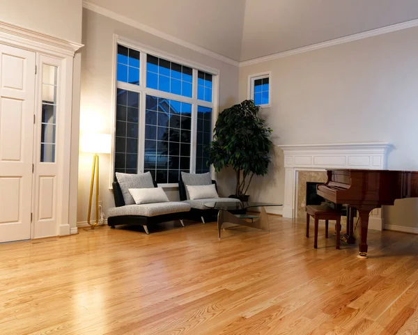 Modern living room with real oak hardwood floors, piano, fireplace and large windows during evening time