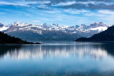 Yaz mevsiminde Alaska Buzul Koyu 'nu geniş açıdan görebiliriz. Bulutlar ve mavi gökyüzü dağların arasında karışıyor.. 