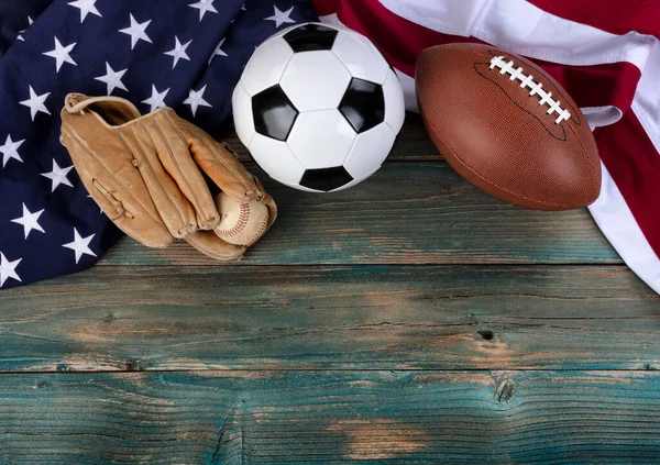 United States flag with soccer ball, baseball and football on faded blue wooden planks for multiple sport concept