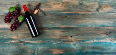 Kırmızı şarap arka planında şişe, üzüm ve soluk mavi tahta üzerinde eski bir tirbuşon var.