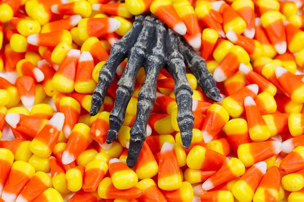 Scary skeleton hand coming out of pile of candy corn — Stock Photo, Image