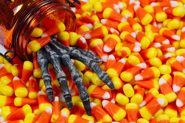 Scary skeleton hand coming out jar into a pile of candy corn — Stock Photo, Image