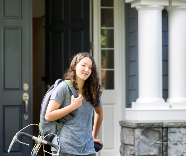 Teenage girl outdoors with school bag and bicycle in front of ho — Stock Photo, Image