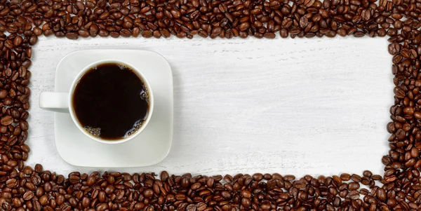 Frischer dunkler Kaffee umgeben von gerösteten Kaffeebohnen — Stockfoto