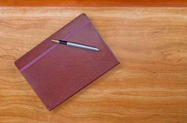 Bloco de notas de couro com caneta na área de trabalho de madeira cereja — Fotografia de Stock