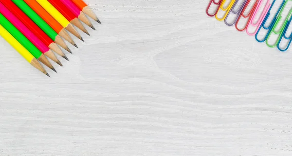 Bright colorful pencils and paper clips on white wooden desktop — Stock Photo, Image