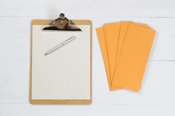 Clipboard em branco com caneta de prata e envelopes na área de trabalho branca — Fotografia de Stock