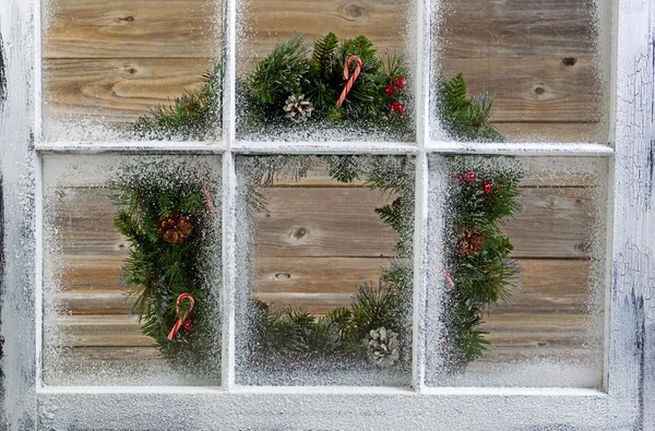 Snow covered window with decorative Christmas wreath on window — Stock Photo, Image