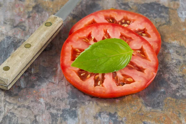 Single basil leaf and sliced tomato with knife on real stone boa — Stock Photo, Image