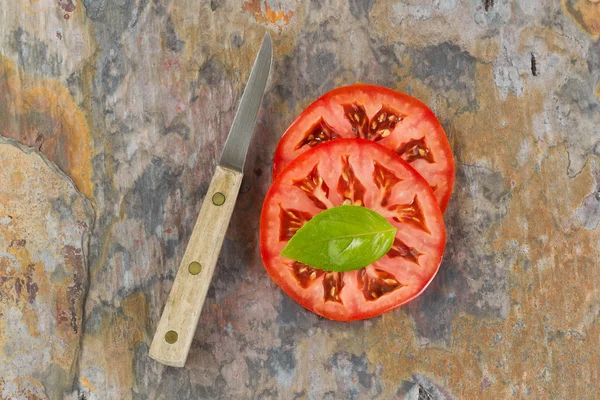 Folha de manjericão e tomate fatiado com faca na placa de pedra real — Fotografia de Stock