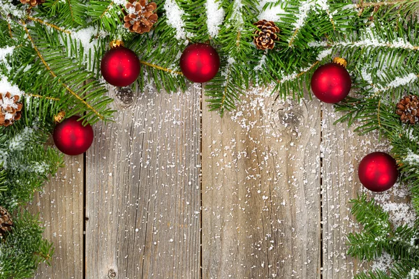 Sneeuw bedekt fir takken met rode ornamenten en kegels op rustieke — Stockfoto
