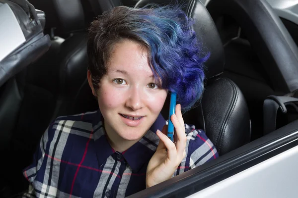 Smiling teenage girl seating in car while talking on cell phone — Stock Photo, Image