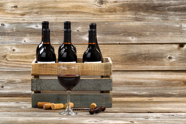 Glas rode wijn en volledige flessen in houten kist op rustieke woode — Stockfoto