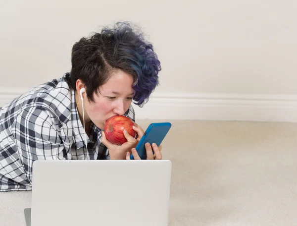 Девочка-подросток ест яблоко, пользуясь мобильным телефоном и слушает — стоковое фото