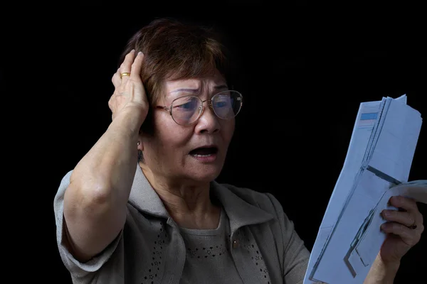 Femme âgée stressée par les factures financières sur fond noir — Photo