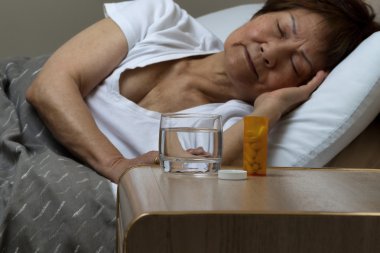 Bottle of medicine and water with senior woman sleeping in backg