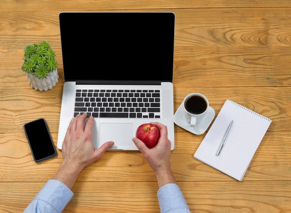 Männliche Hand hält Apfel, während sie Laptop benutzt — Stockfoto