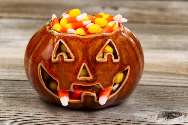 Spooky fanged pumpkin filled with candy corn on rustic wood — Stock Photo, Image