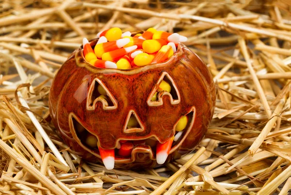Spooky pumpkin filled with candy corn on straw — Stock Photo, Image