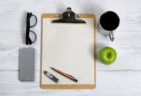 Clipboard with office supplies and snack foods on a white wooden