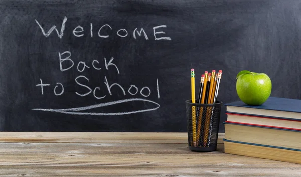 Old wooden desktop with simple school supplies and blackboard — Stock Photo, Image