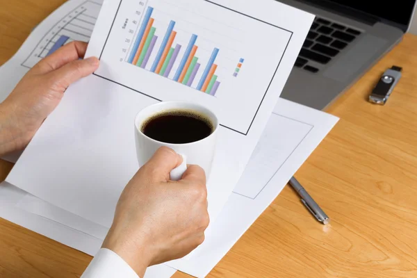 Vrouwelijke hand met een kopje koffie bij het bekijken van financiële ch — Stockfoto